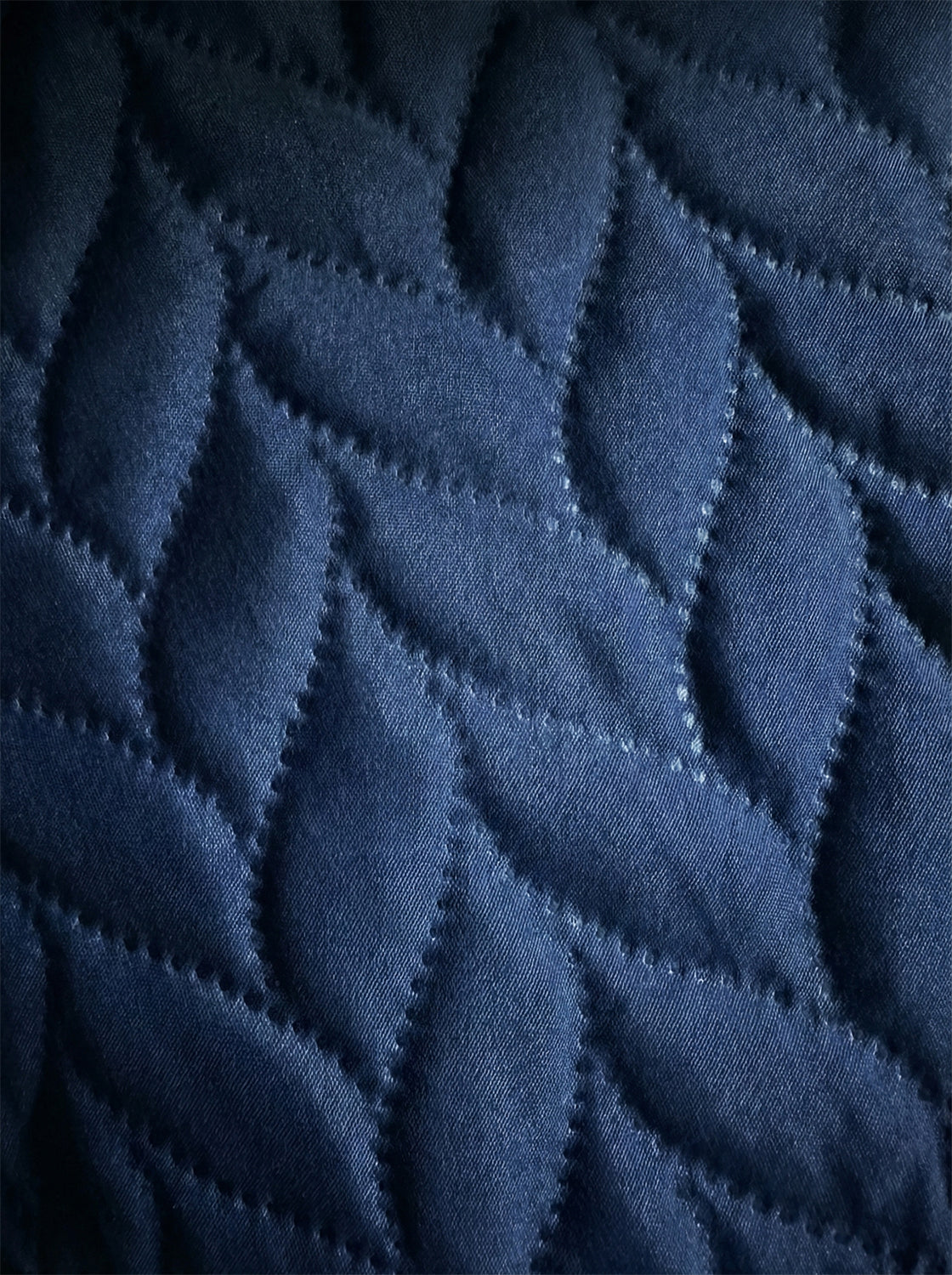 Close-up of quilted dark blue cotton bedding with leaf pattern stitching