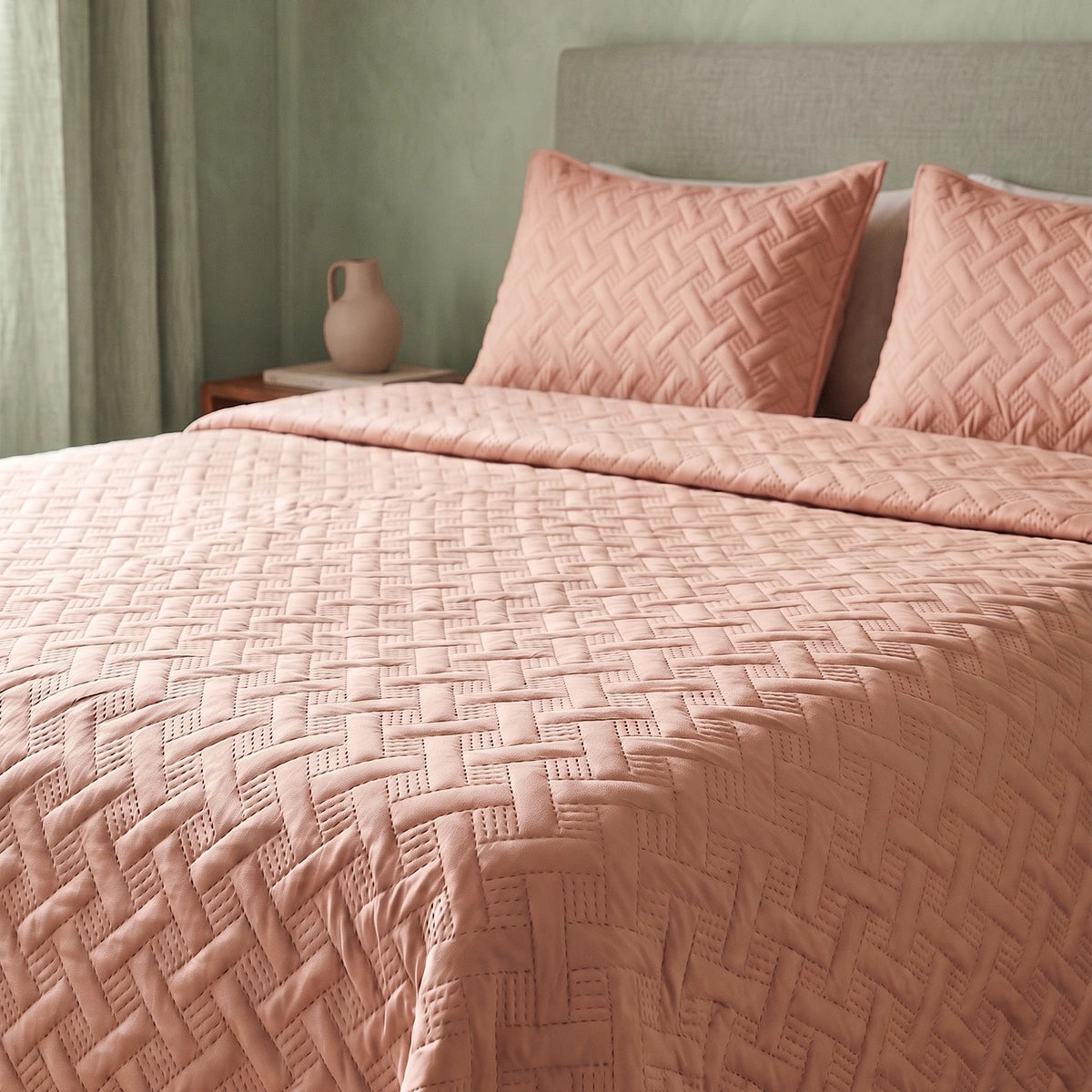 Angled view of soft rose woven lattice quilted bedspread showing full bed styling against a green wall