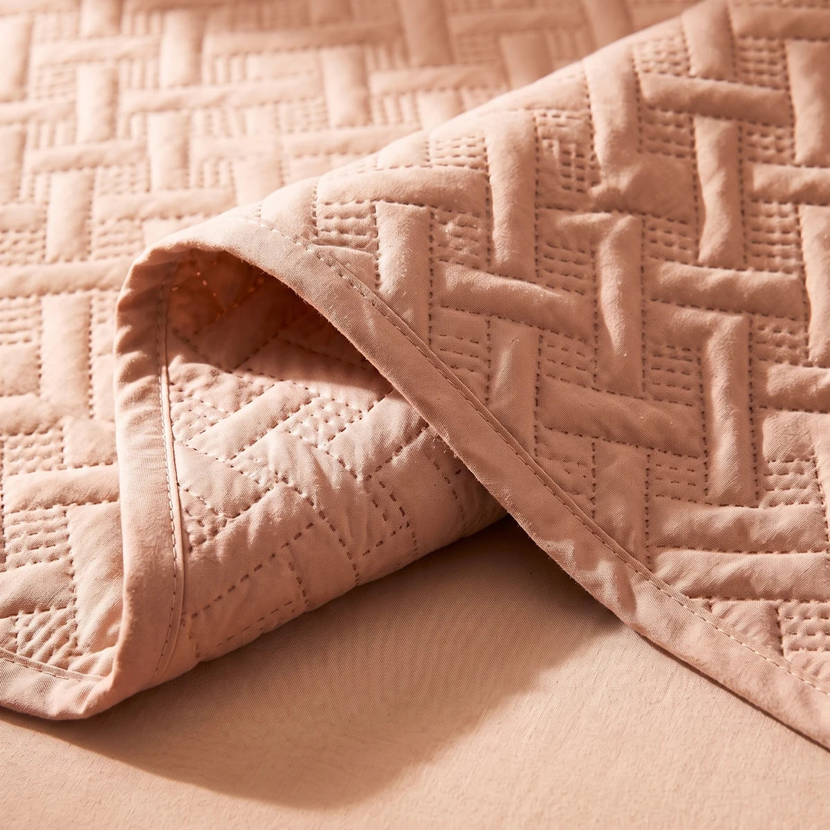 Close-up of embossed woven lattice pattern and stitch detail on soft rose fabric bedspread