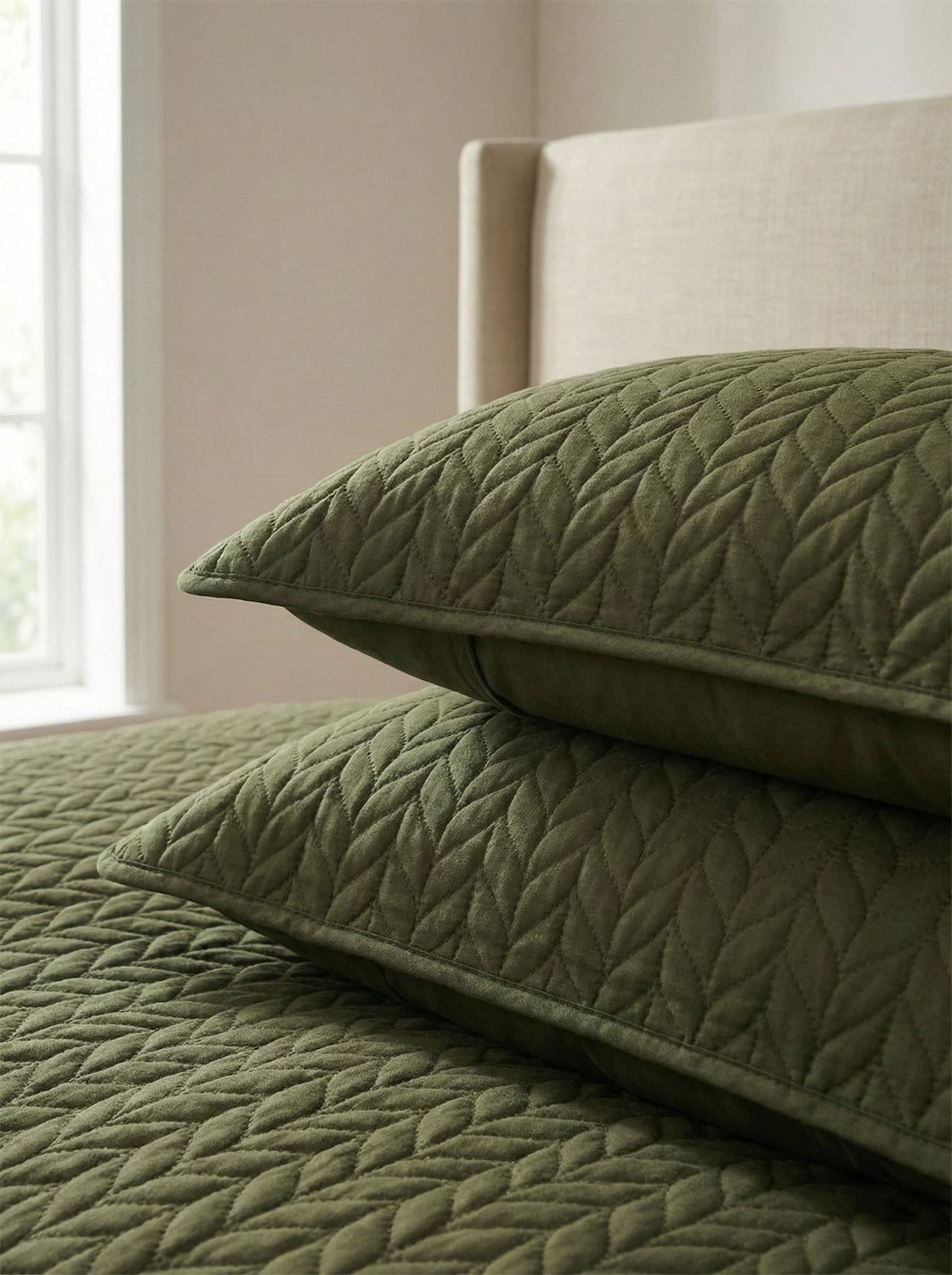 Olive green quilted pillows and bedding with a leaf pattern on a modern bed