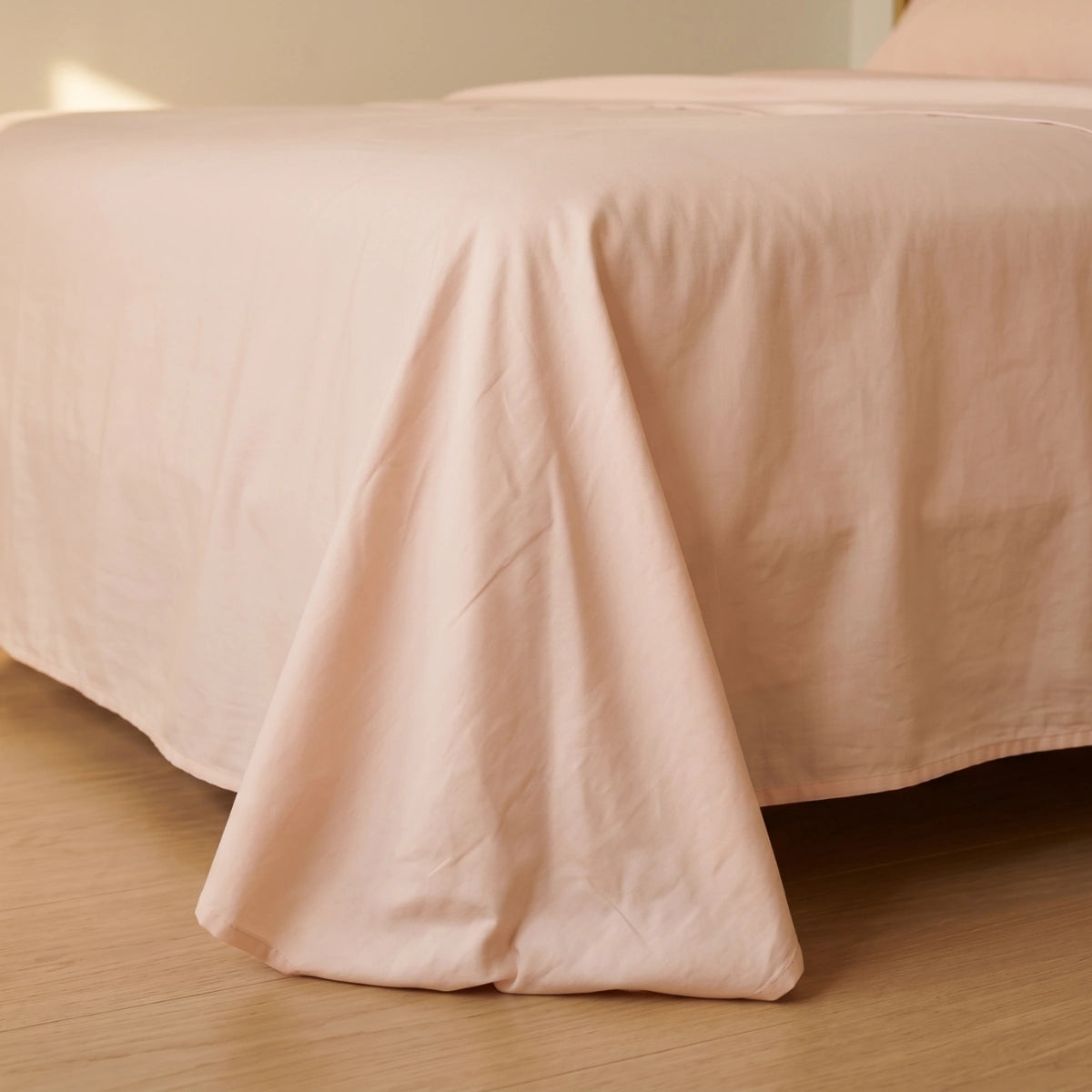 Pink cotton bedsheet draping naturally over bed corner showing fabric weight and generous sizing